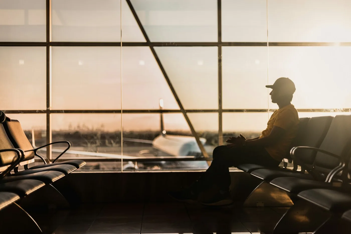Silhouette of a traveler sitting and waiting near a terminal window at sunset