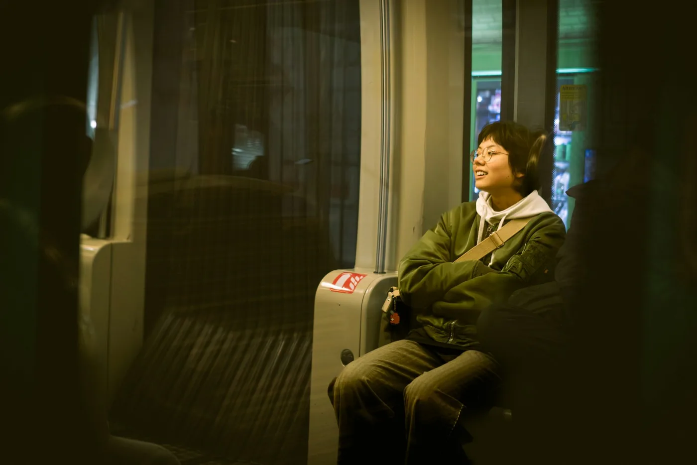 Traveler in a green jacket with a suitcase sitting by a train window at night with their eyes closed