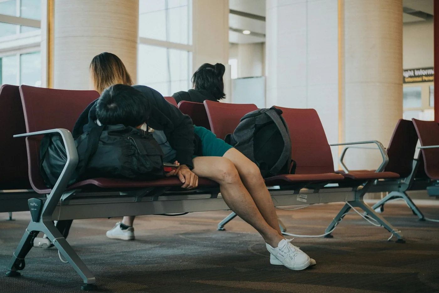 Reisende ruhen sich auf Flughafenbänken mit ihren Taschen aus, von hinten gesehen