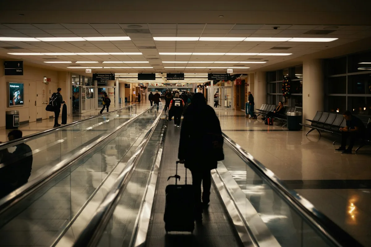 A traveller pulling a small carry-on along a moving walkway in a dark airport hall