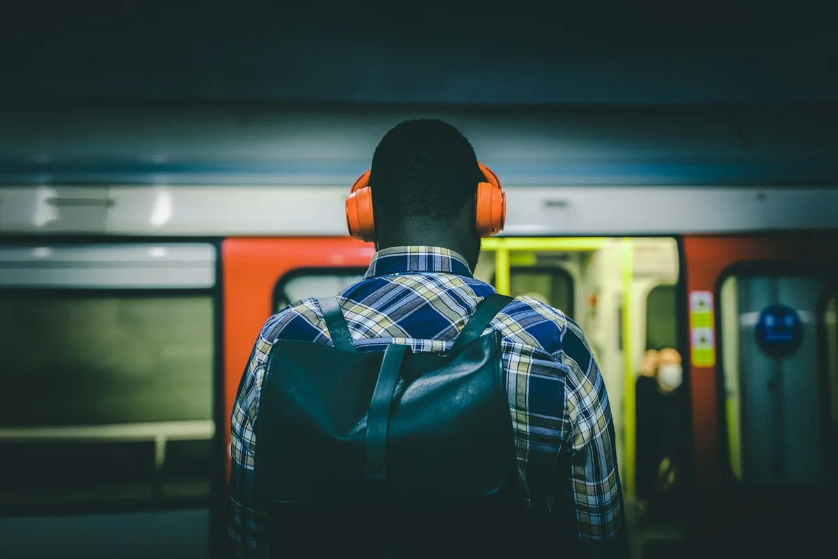 A traveller with orange over-ear headphones and a backpack waiting on a metro platform
