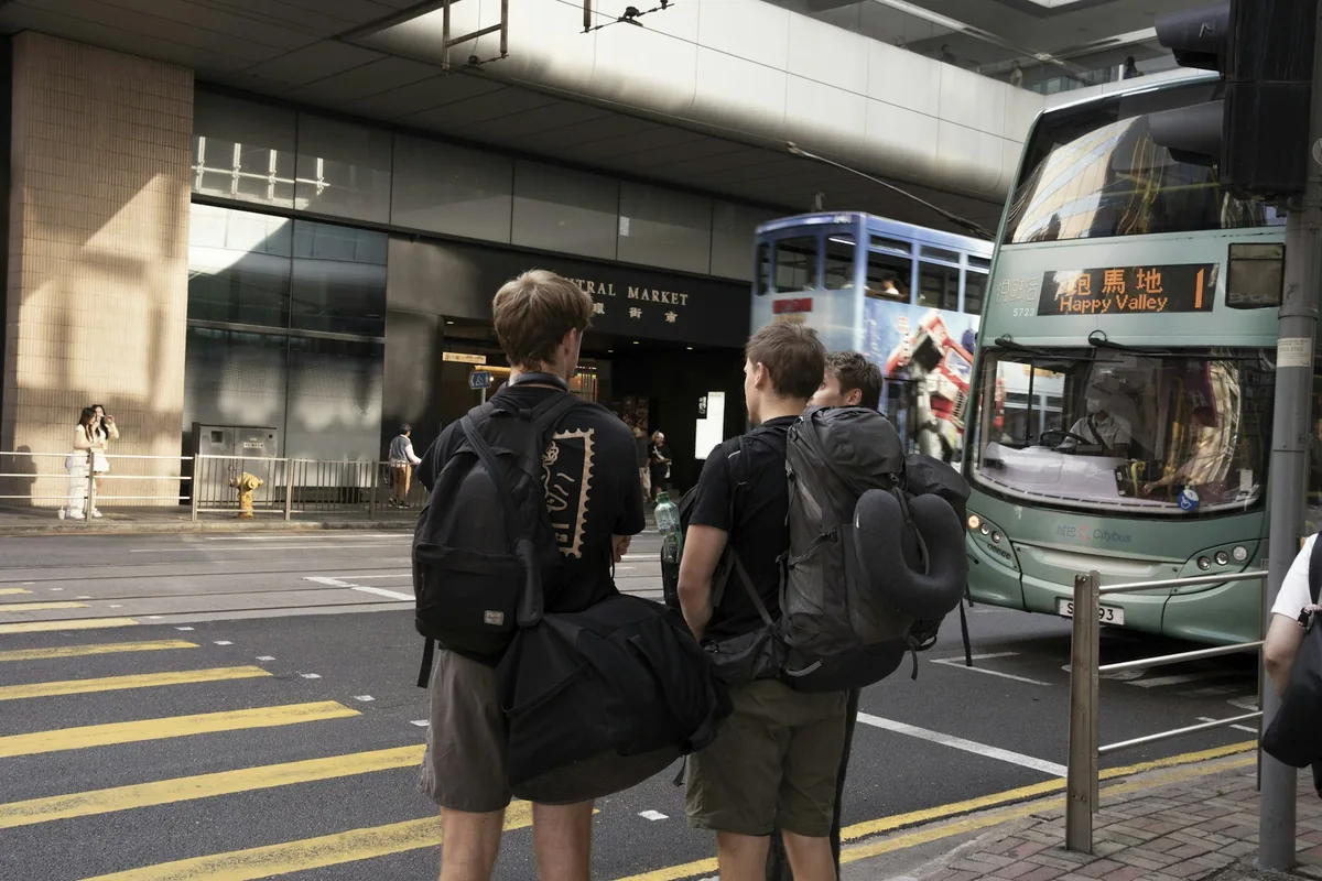Two travellers with backpacks waiting at a crosswalk in Hong Kong next to a tram