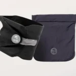 Black Trtl travel pillow shown next to its matching dark carry bag with a carabiner