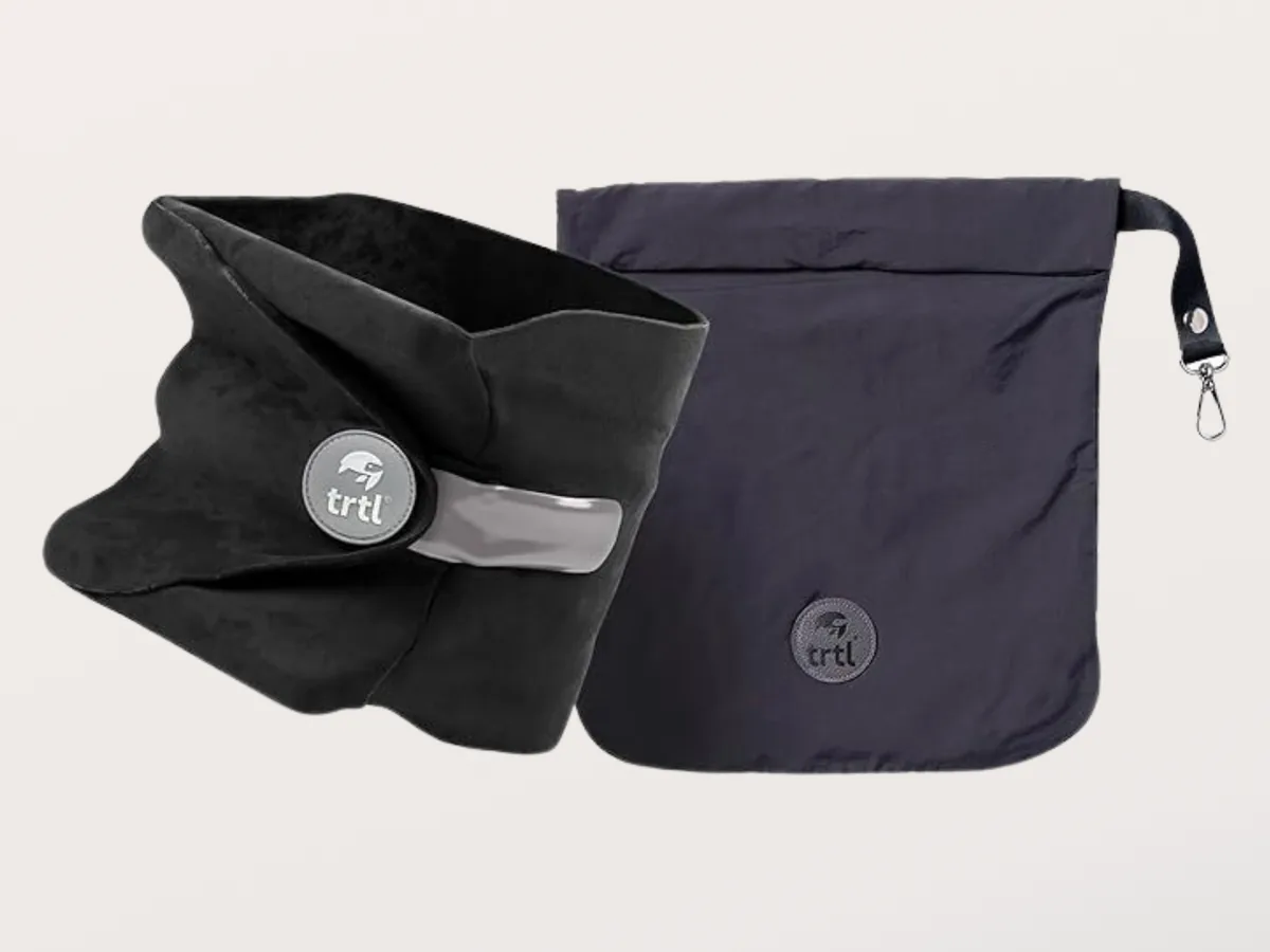 Black Trtl travel pillow shown next to its matching dark carry bag with a carabiner