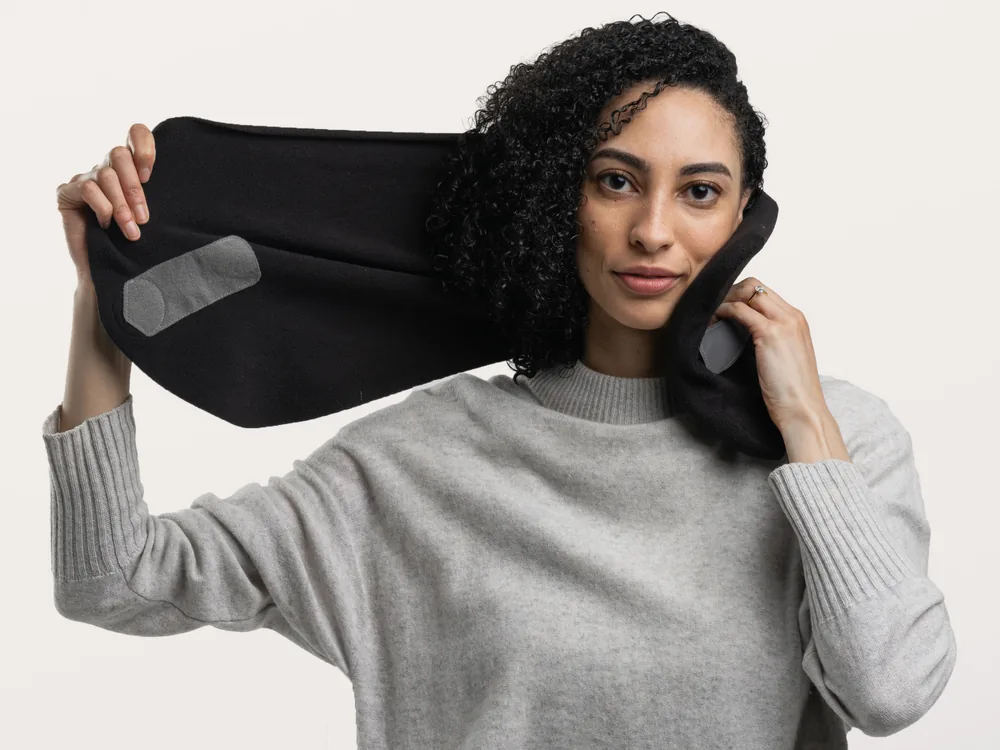 Woman holding a black Trtl travel pillow wrapped against her neck like a scarf