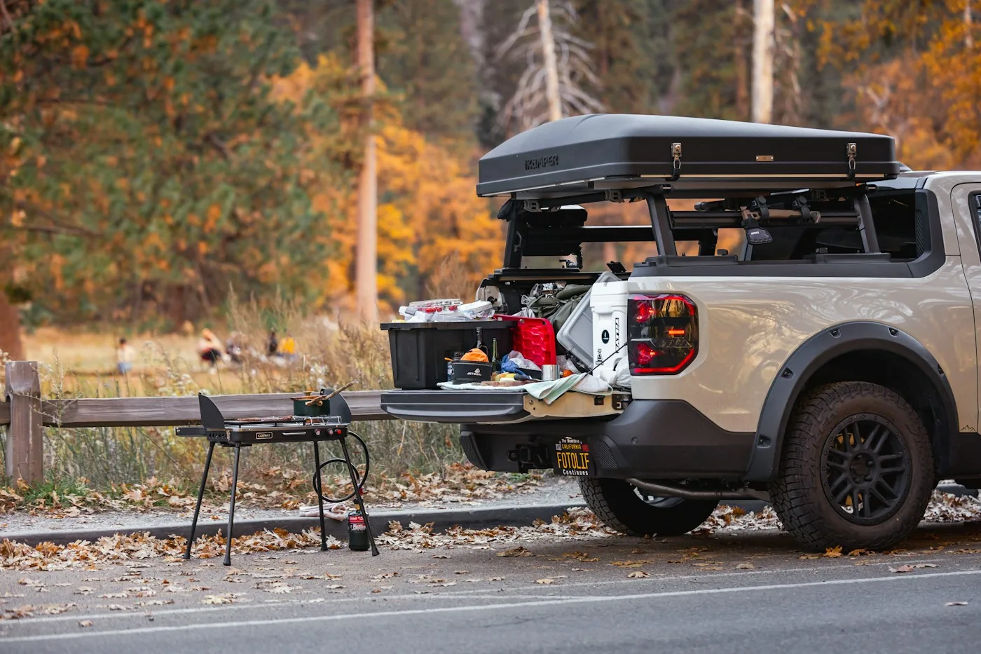 Pickup with an open tailgate, a camp table and cooking gear at an autumn roadside stop