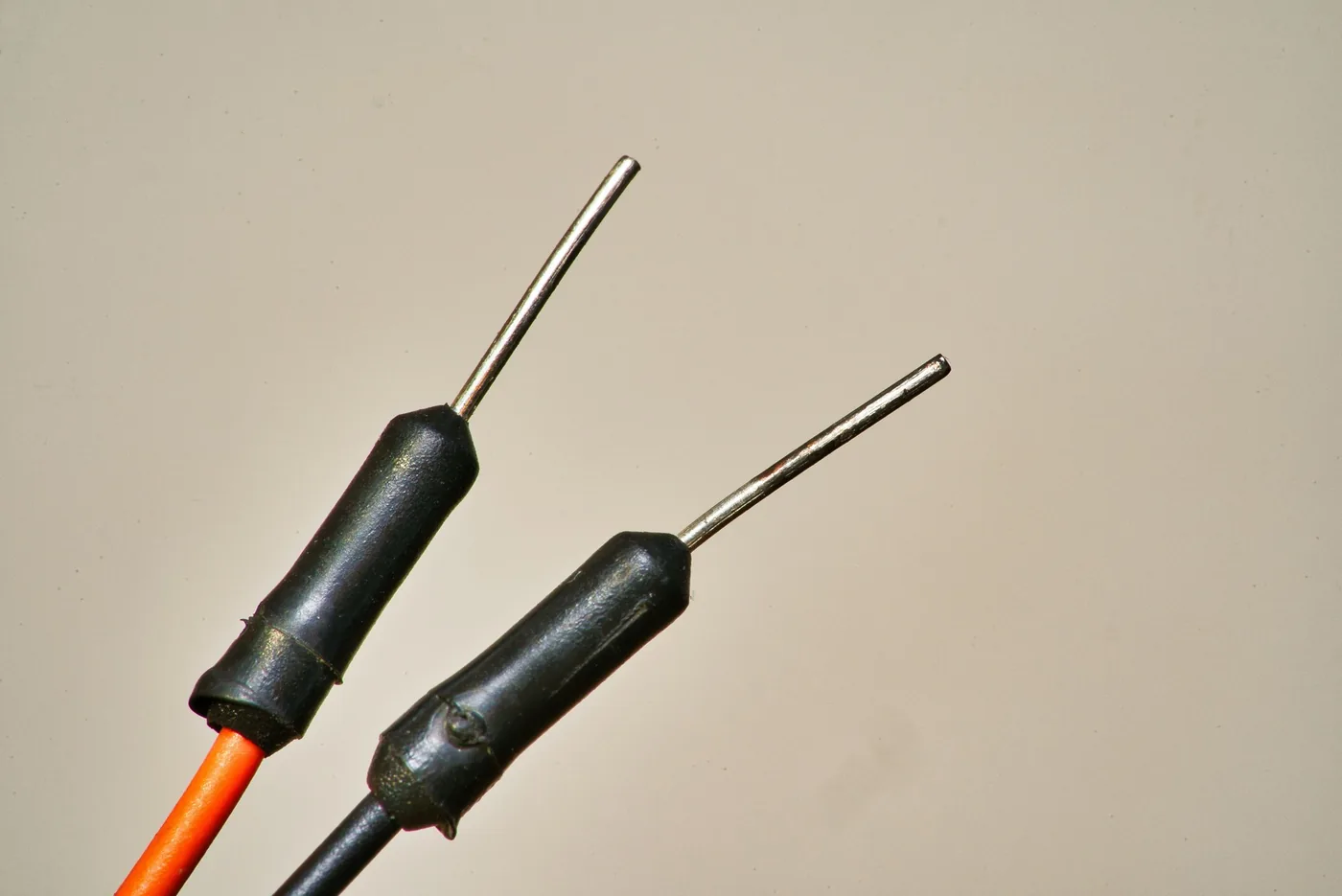 Dos cables eléctricos con los extremos de metal expuestos y aislamiento negro sobre un fondo liso