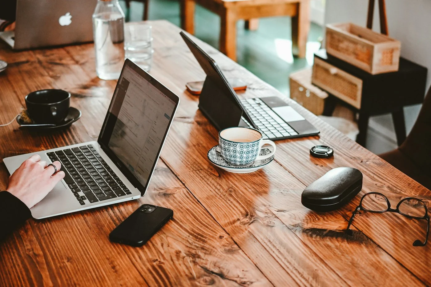 Two laptops and coffee cups on a wooden cafe table with a phone and glasses