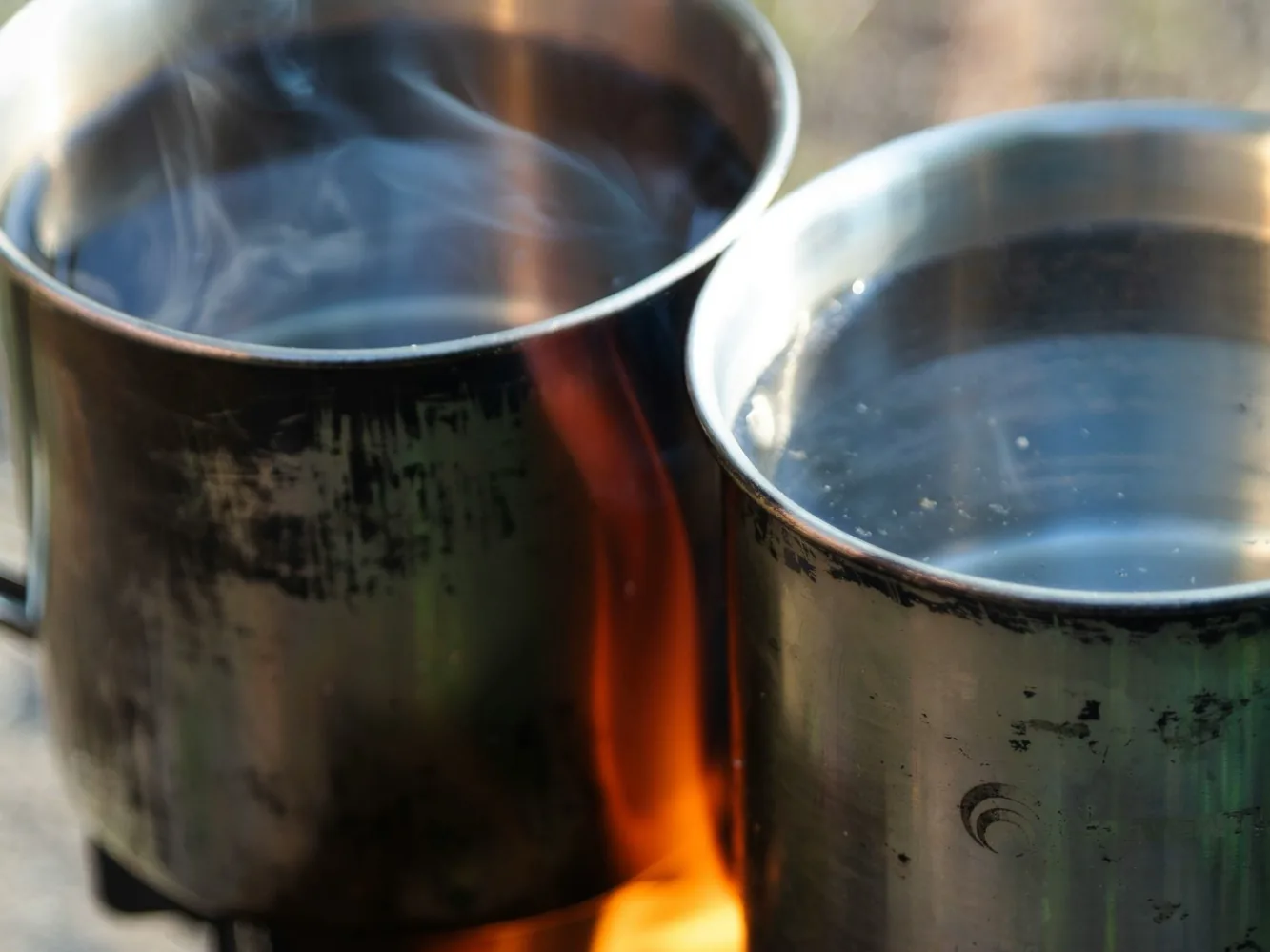 Zwei Metalltöpfe mit Wasser werden über einem offenen Feuer erhitzt