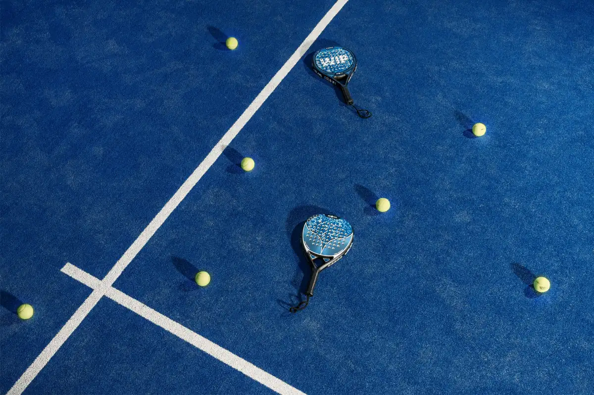 Dos palas de pádel y pelotas de tenis sobre una pista azul de pádel con líneas blancas