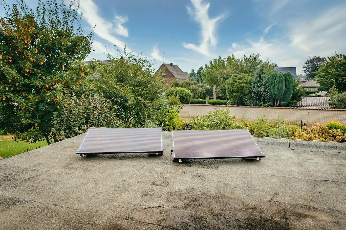 Zwei Solarpanels liegen flach auf einem Dach, im Hintergrund grüne Bäume und klarer Himmel