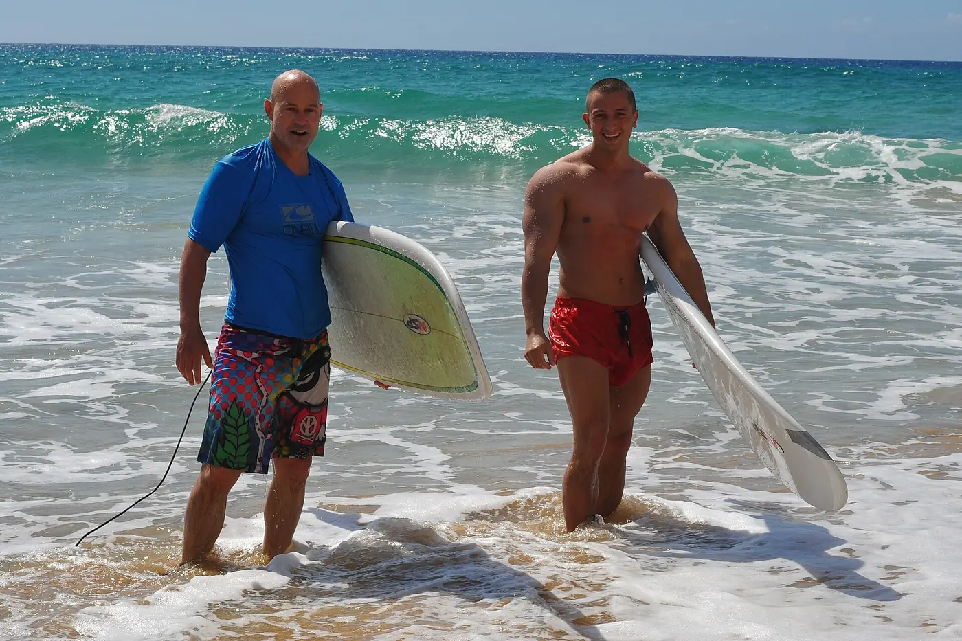 Two surfers walking out of the shallows with their boards after a lesson