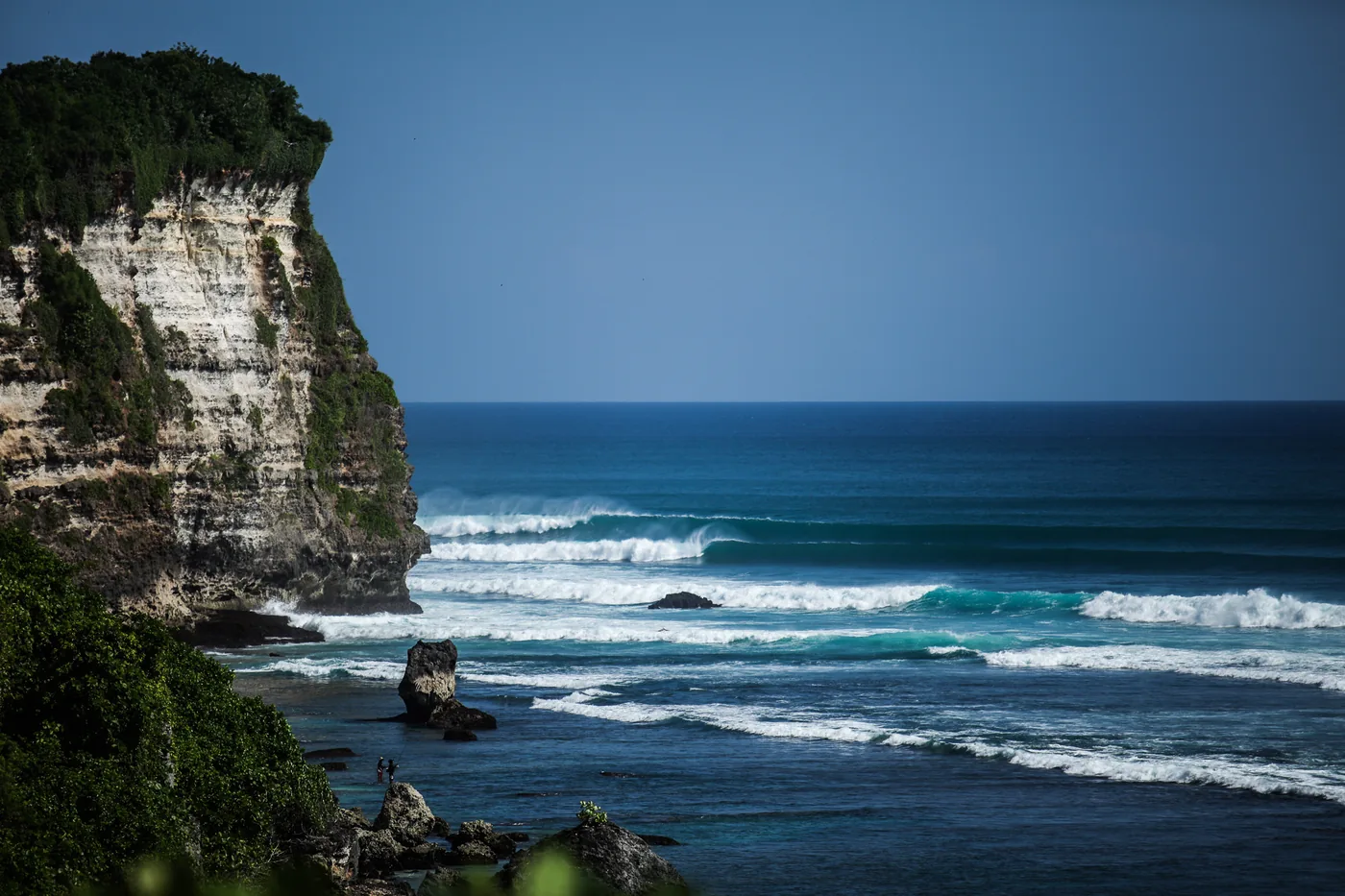 Limestone cliff above the sea with long waves peeling along the Uluwatu reef, Bali