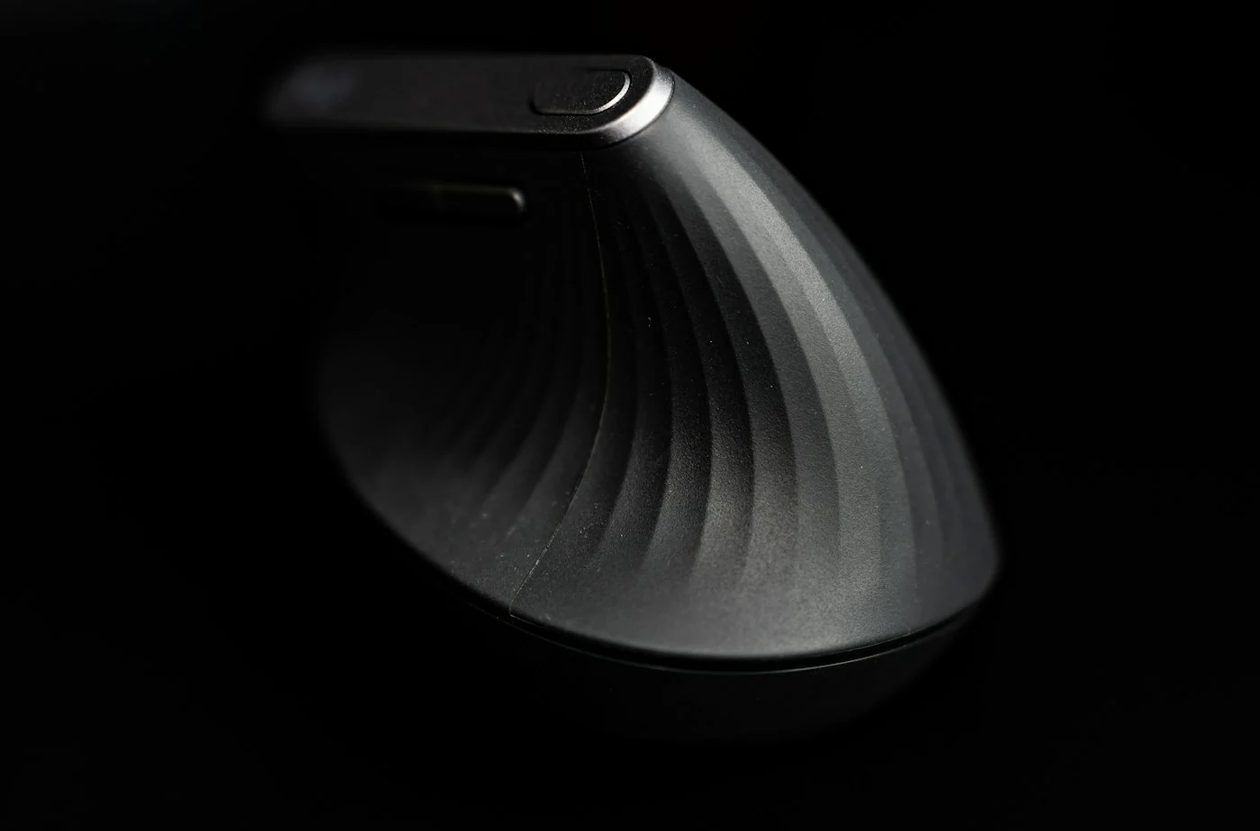 Black vertical ergonomic mouse with a ridged grip against a dark background