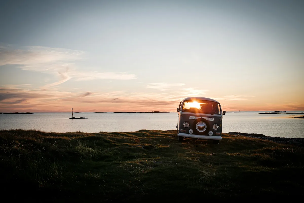 A vintage camper van parked by the ocean at sunset