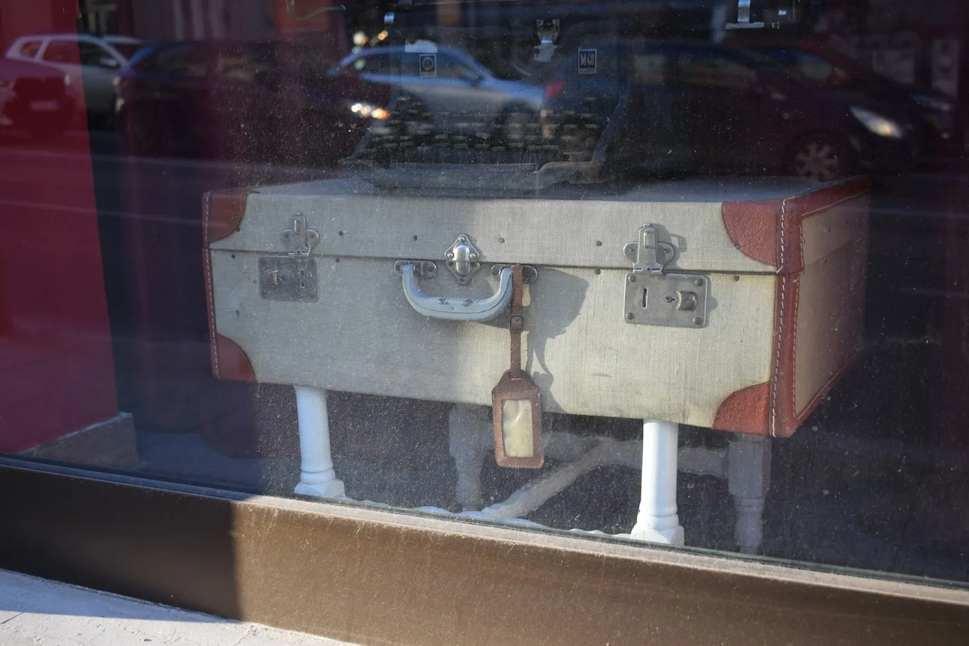 Vintage cream suitcase with a luggage tag standing behind a shop window