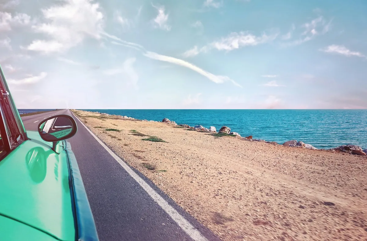 Vintage turquoise car on a quiet road next to a sandy beach