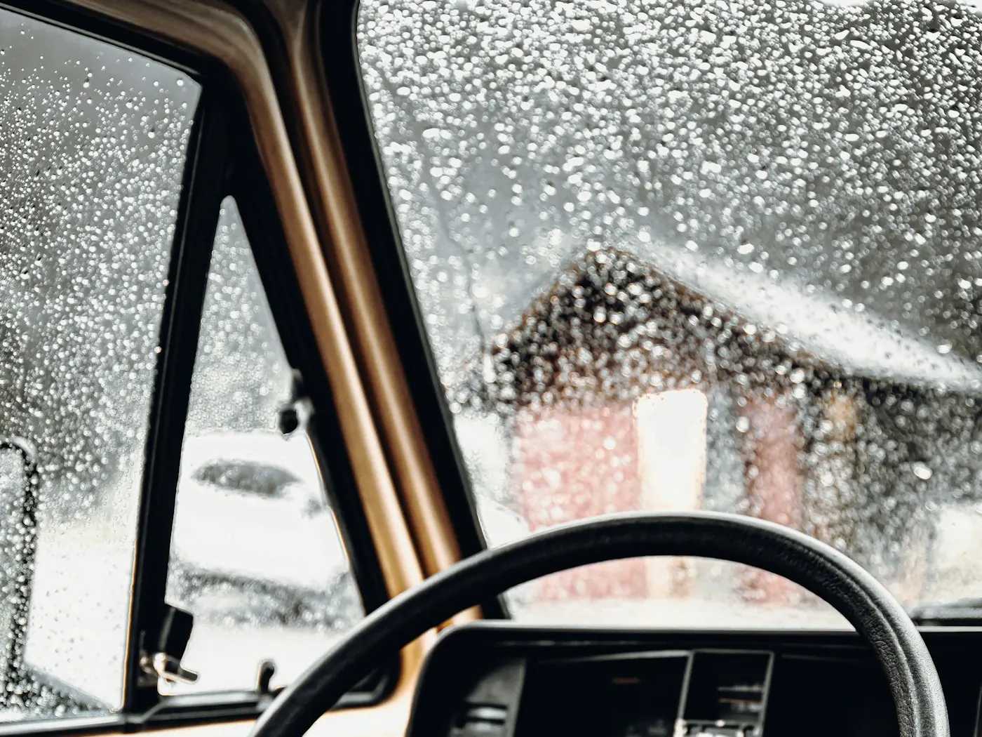 Lenkrad und Fenster eines alten VW-Campingbusses mit Regentropfen auf der Scheibe