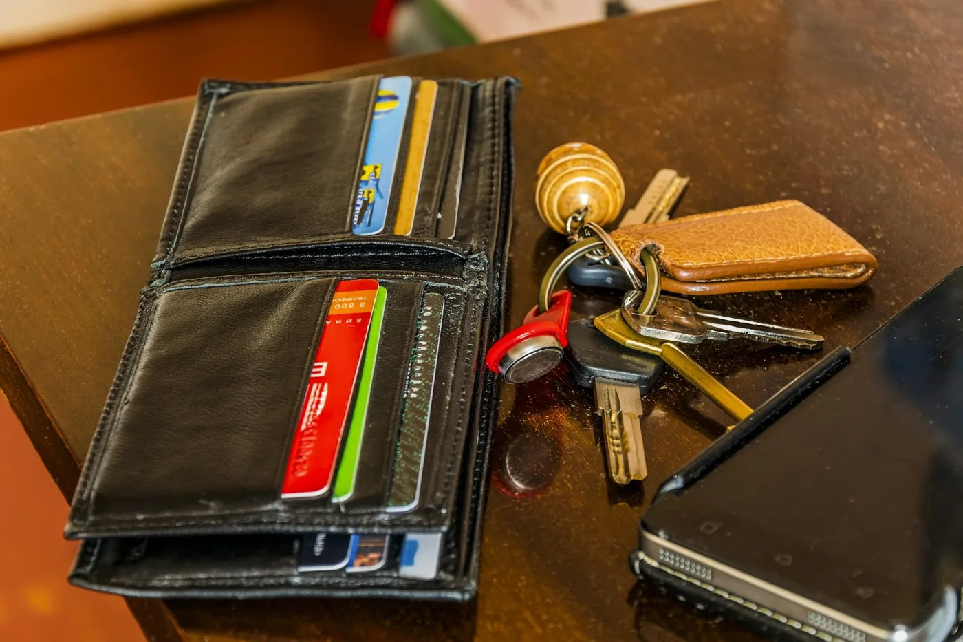 Open black leather wallet with cards and a bunch of keys on a wooden table