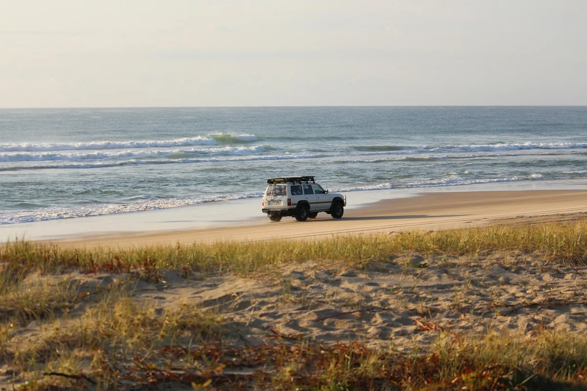 White four-wheel-drive car parked on a sandy beach at the water edge