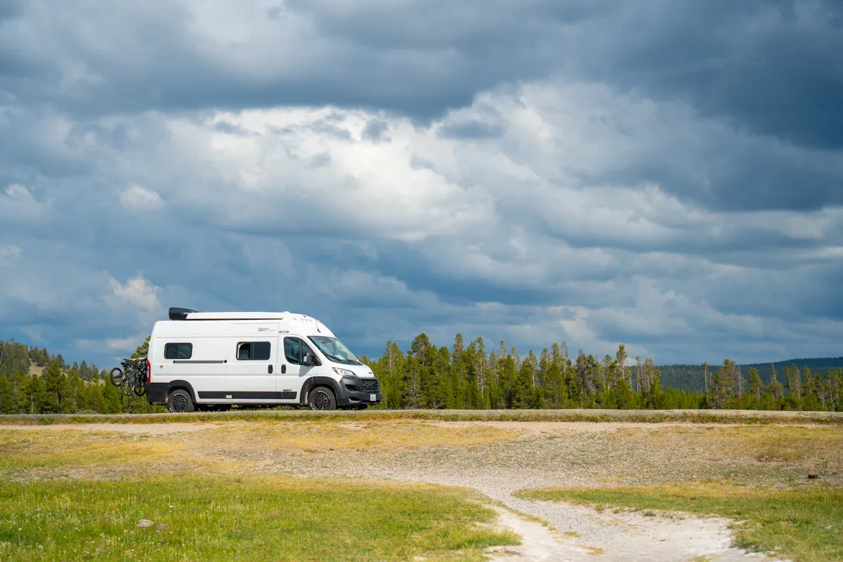 Een witte camper geparkeerd naast een grindweg onder een bewolkte hemel
