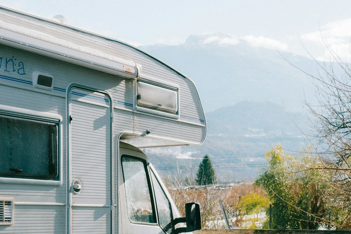 Weißer Camper mit vereisten Fenstern, im Winter vor verschneiten Bergen geparkt