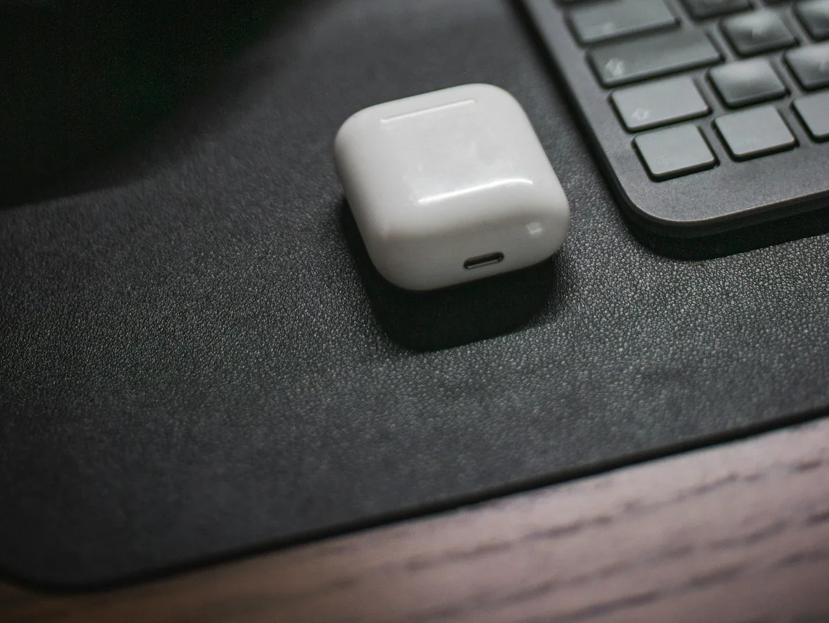White wireless earbuds case on a dark desk mat next to a keyboard