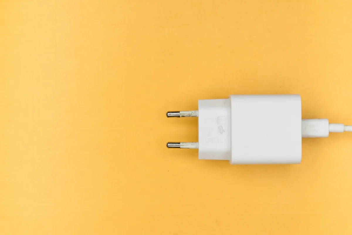 A white two-pin European plug adapter with a cable on a yellow surface