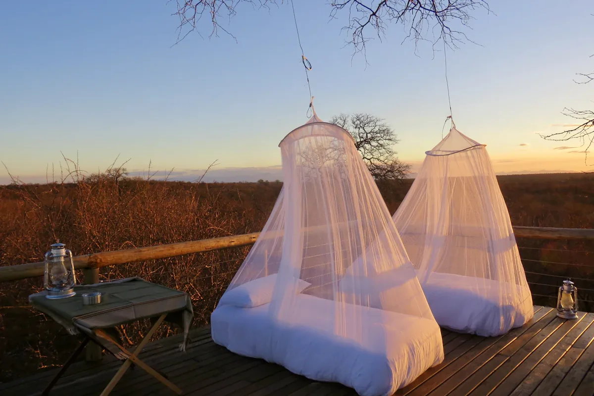 Two white hanging mosquito nets over beds on a wooden deck at sunset