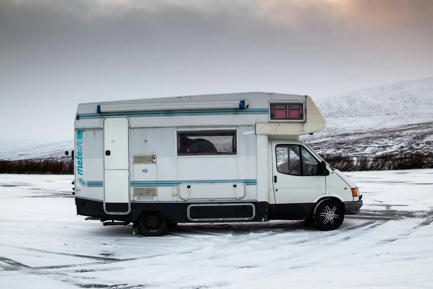 White motorhome parked on a snowy plain with a hill behind it under a grey sky