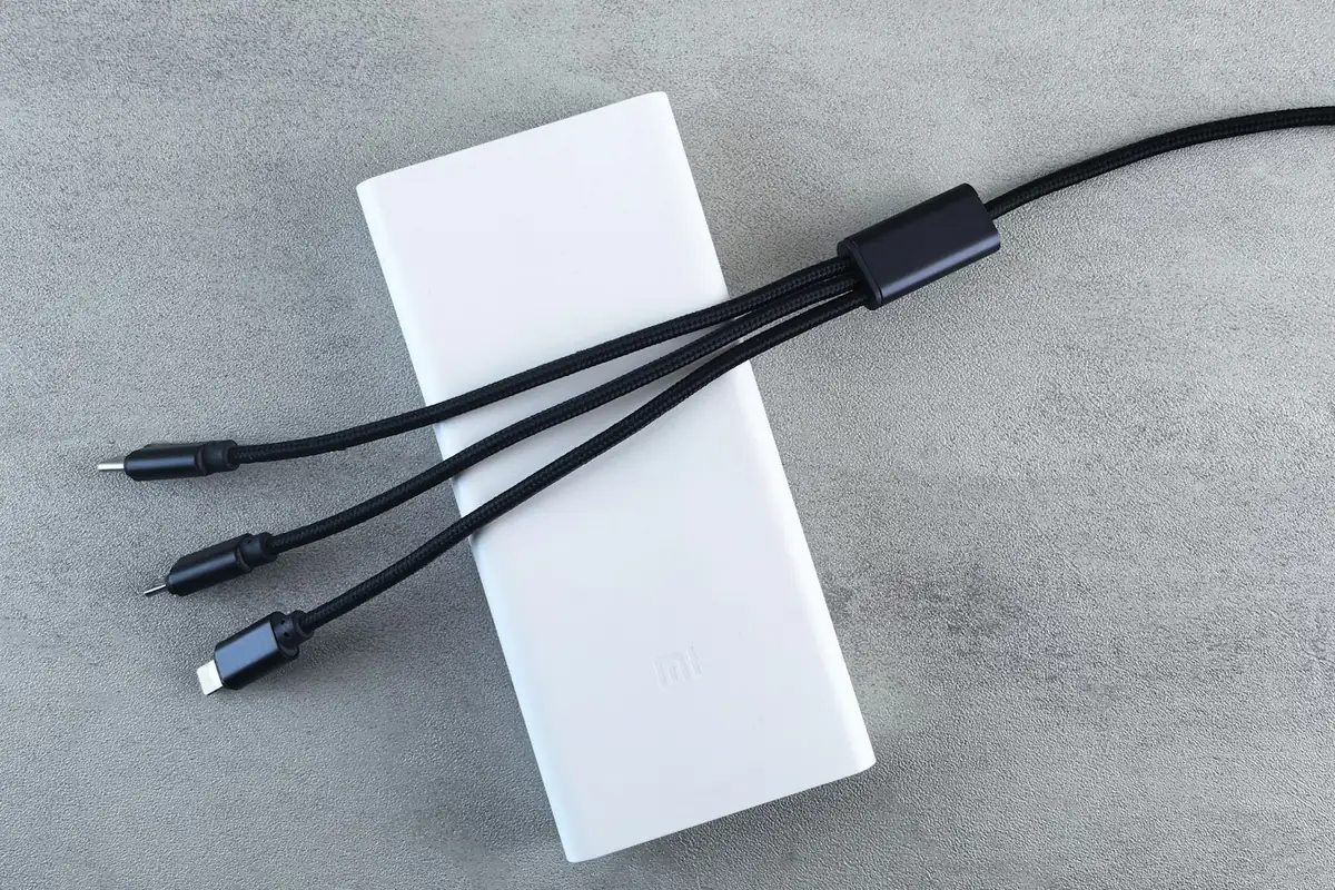 A white power bank on a grey surface with three charging cables attached