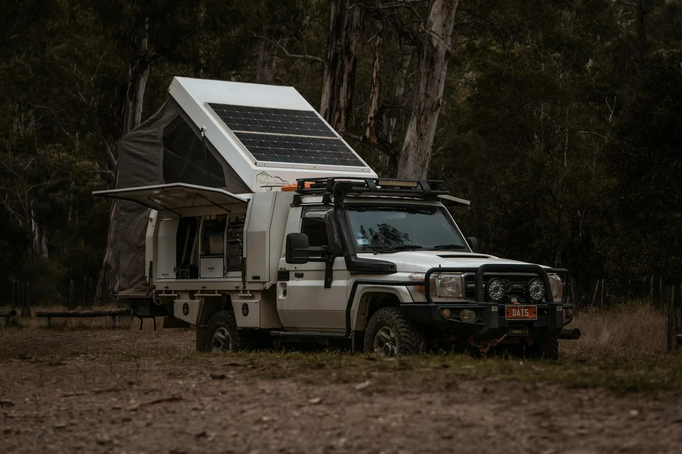 White truck camper in a dark forest with a solar panel tilted on the roof
