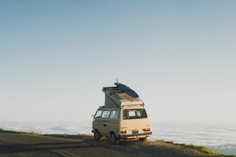 A camper van with a roof tent parked on a coastal road above the clouds