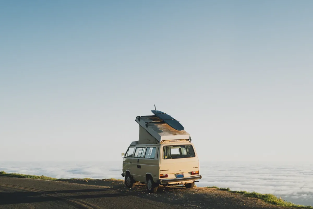 A camper van with a roof tent parked on a coastal road above the clouds