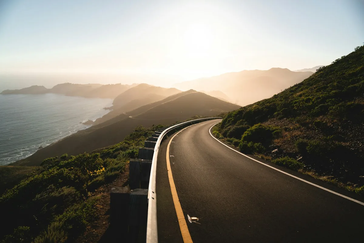 Winding road curving along a green hillside above the ocean