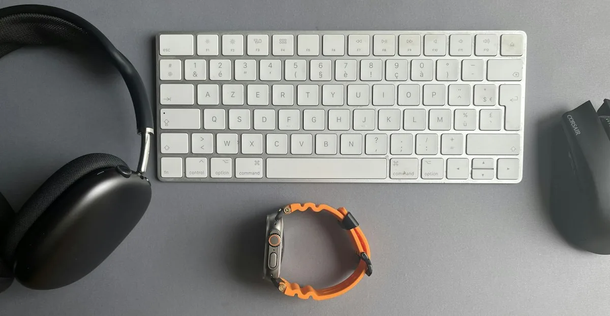 Wireless keyboard, black headphones and a mouse laid out on a grey desk