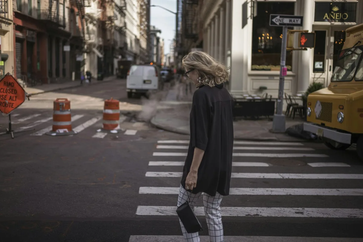 A woman crossing a city street at a crosswalk with a yellow taxi behind her
