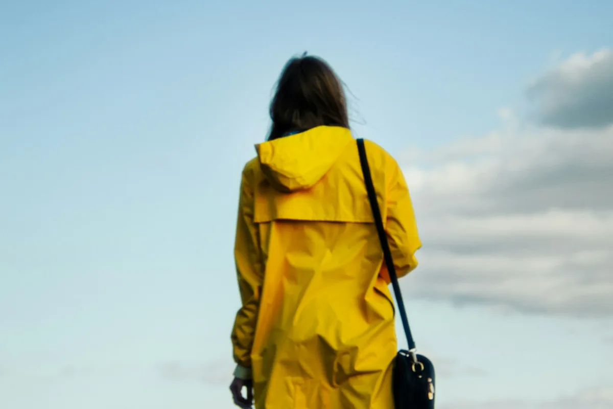 A woman in a yellow raincoat standing on a ledge above a city