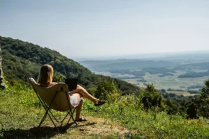 A woman working on a laptop in a camping chair on a mountain overlook