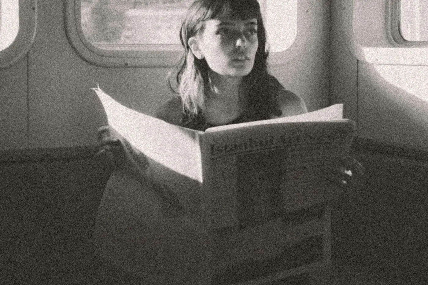 A woman reading a large newspaper in an old train compartment, in black and white