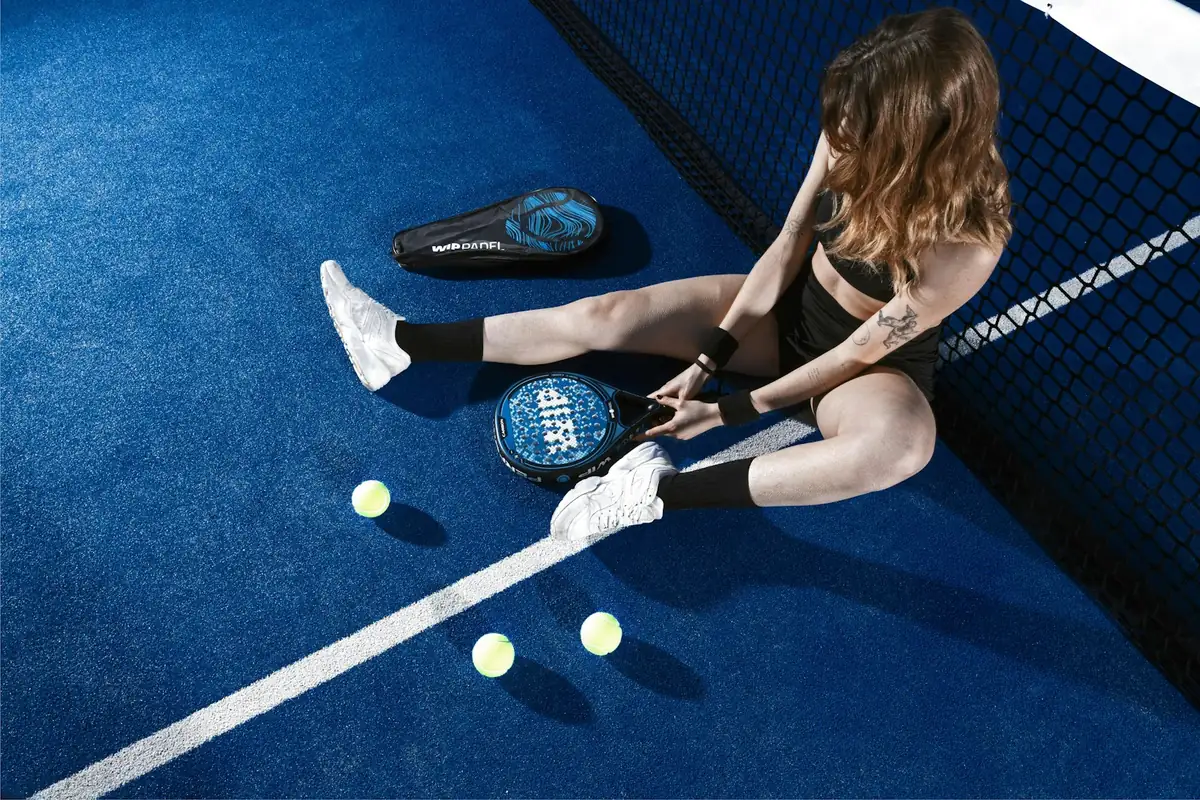 Mujer sentada en una pista de pádel azul con una pala y bolas a su alrededor