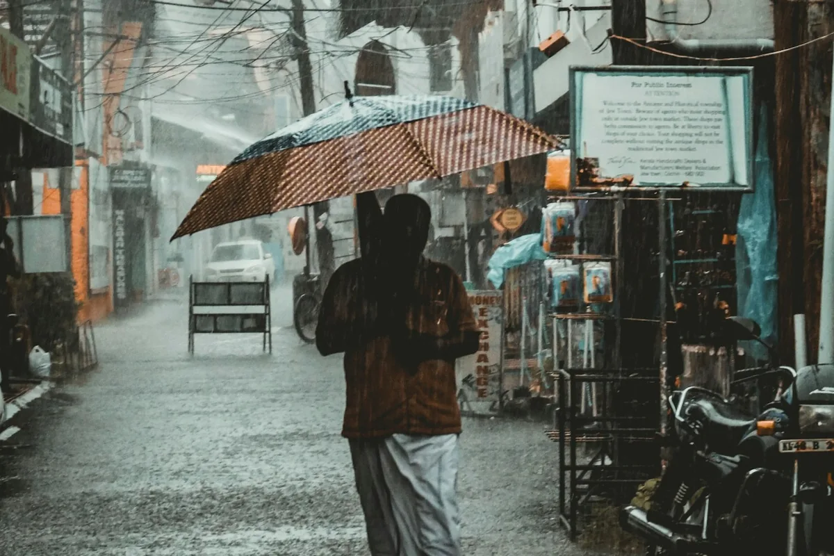 Een vrouw met een paraplu loopt door een natte grijze steeg in de regen
