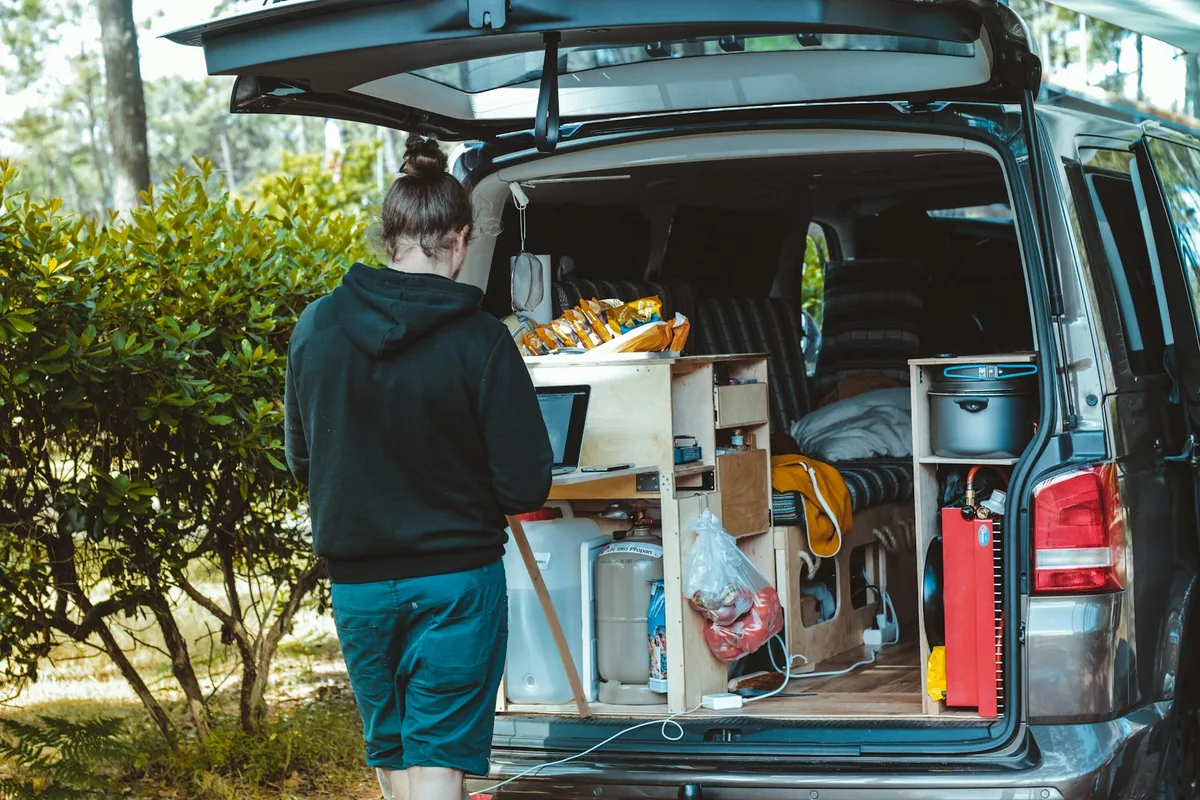 A woman working at the open back of a van with a built-in kitchen