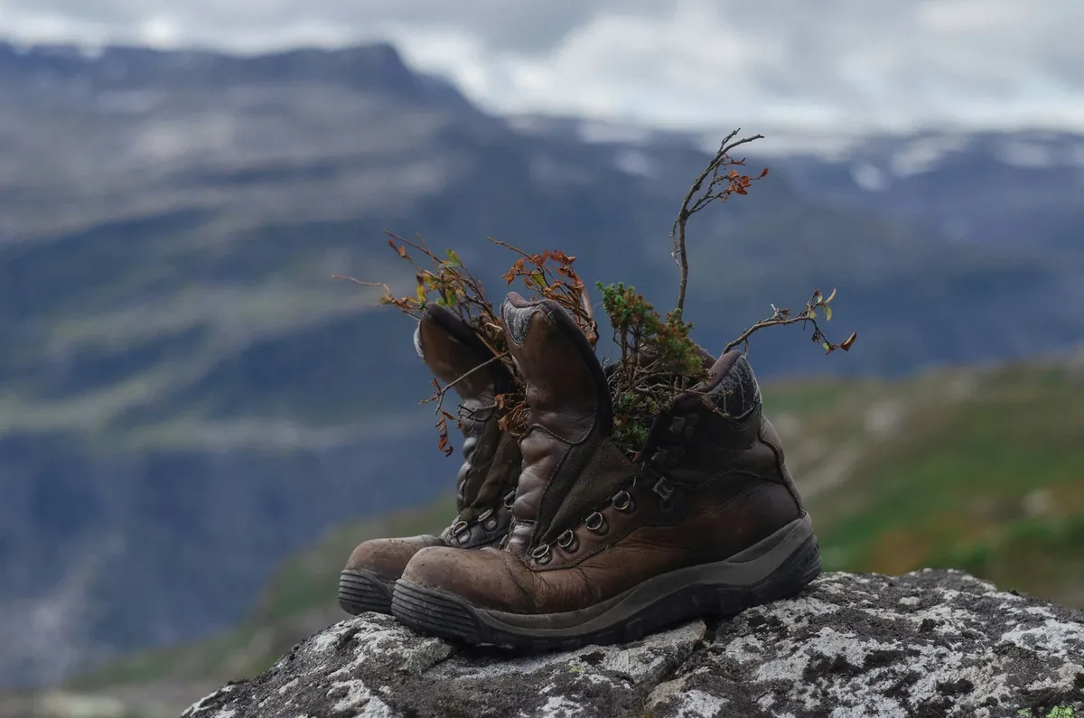 Worn hiking boots on a rock Worn leather hiking boots on a rock with a mountain view behind them