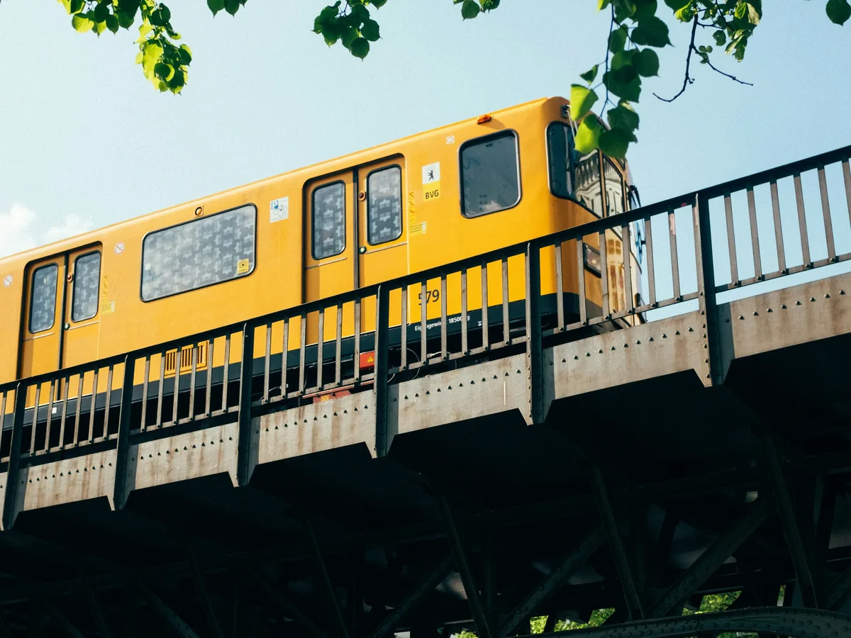 Yellow Berlin U-Bahn train on an elevated track under trees