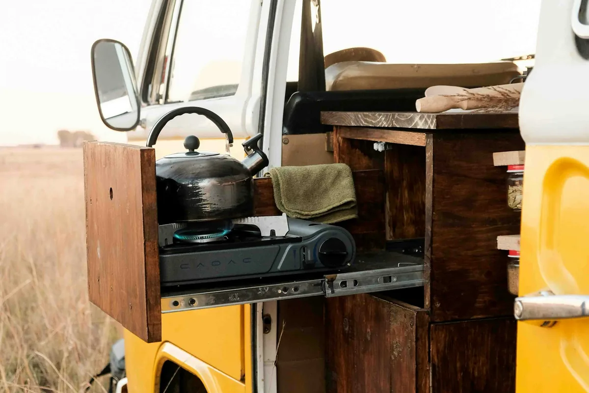 A yellow van with its side door open and a small kitchen with a stove and kettle inside
