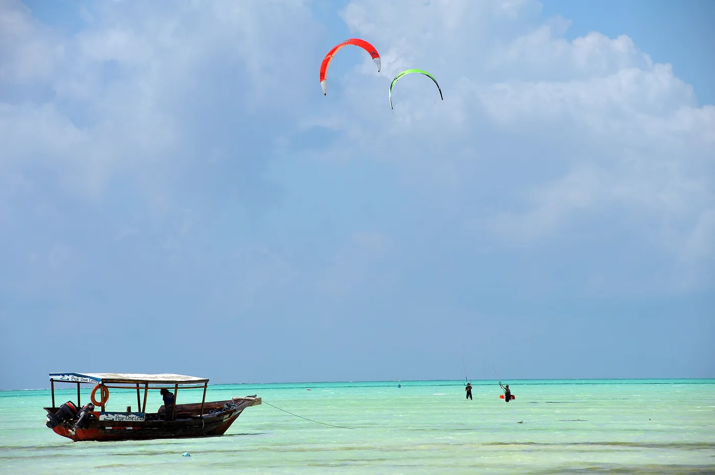 Two kites in the sky over shallow turquoise water and a boat off Zanzibar